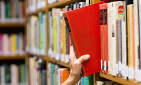 Hand zieht ein rotes Buch aus dem Bücherregal
