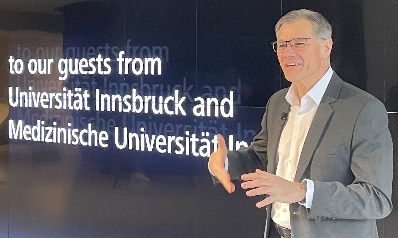 Ein Person mit Brille vor einer Leinwand auf der steht: to our guests from Universität Innsbruck and Medizinische Univeristät Innsbruck