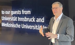 Ein Person mit Brille vor einer Leinwand auf der steht: to our guests from Universität Innsbruck and Medizinische Univeristät Innsbruck