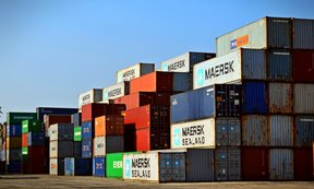 Logistik-Container für Transportschiffe sind auf einer asphaltierten Fläche gestapelt.