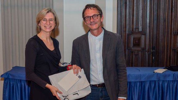 Joanna Chimiak-Opoka, holding an envelope and a bag she received for her achievements, next to Vice Rector Fügenschuh