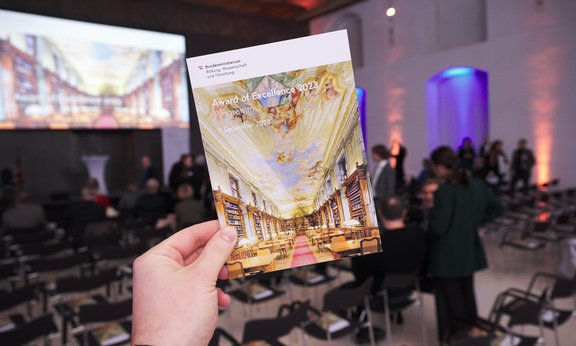 Eine Hand hält eine Broschüre ins Bild