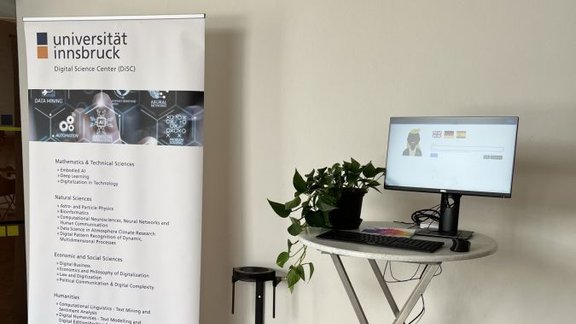 A roll-up with details about the DiSC on the left and a table with a plant and a screen on the right against a white wall.