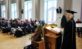 Rektorin Veronika Sexl im Talar spricht am Podium der Aula zum Publikum.