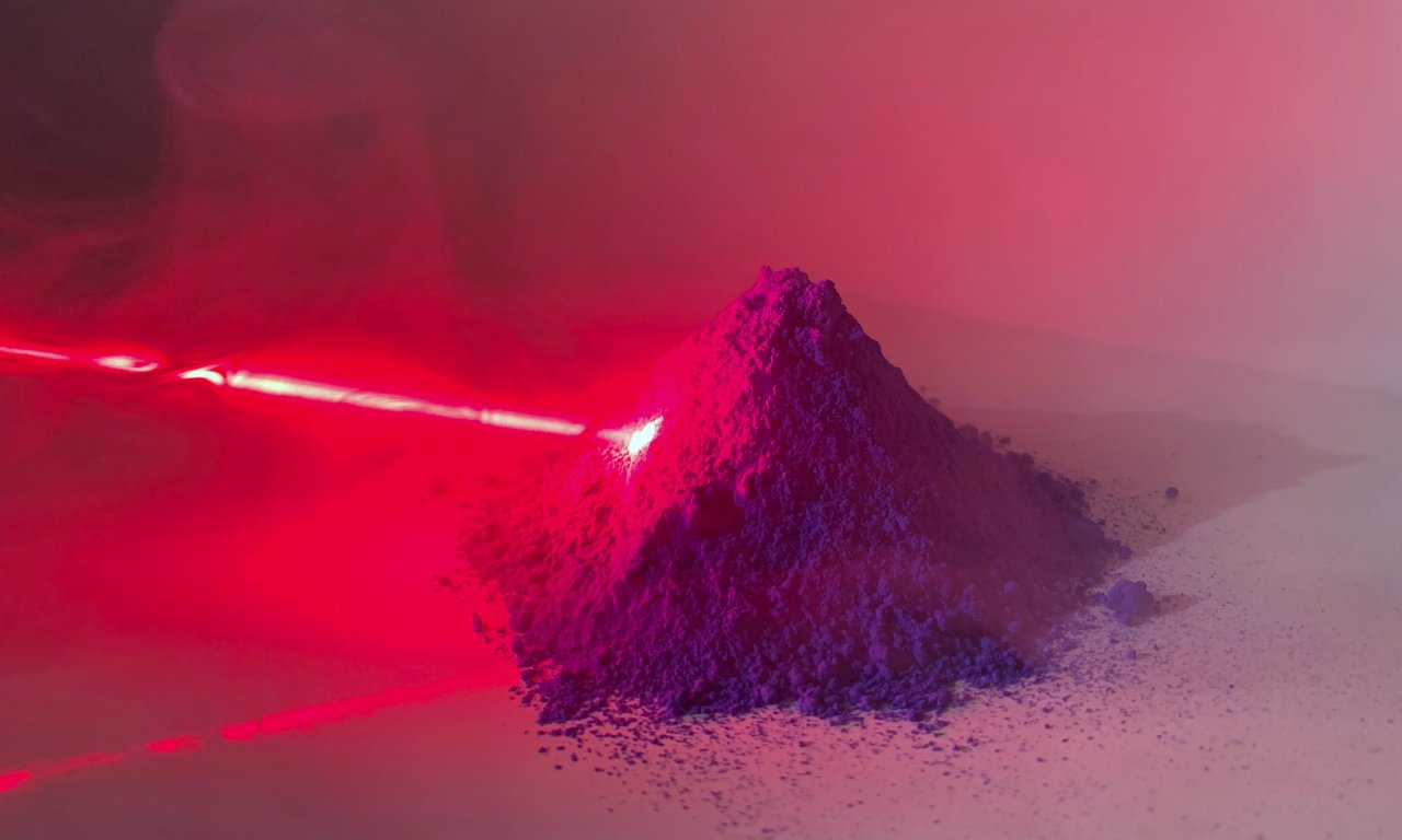 Ein roter Laserstrahl trifft auf einen Häufchen Pulver