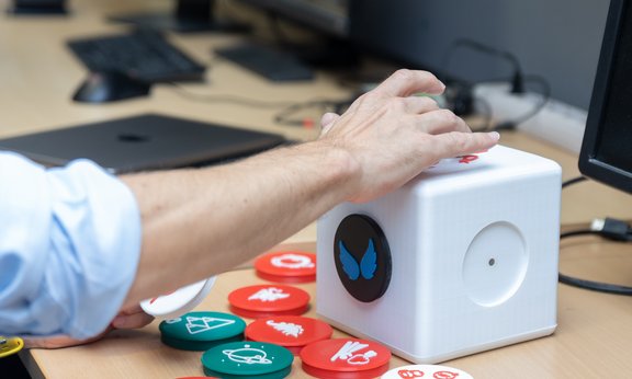 A hand fits round items into wholes in a cube