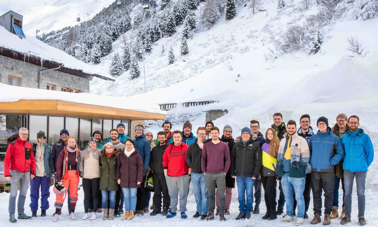 Zahlreiche Personen stehen vor dem Gebäude des Universitätszentrums Obergurgl, dahinter eine schneebedeckte Landschaft