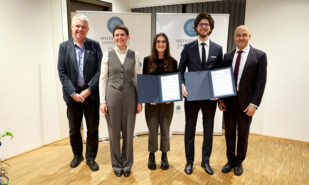 Fünf Personen stehen in einer Reihe, zwei halten eine Urkunde in der Hand.