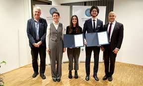 Fünf Personen stehen in einer Reihe, zwei halten eine Urkunde in der Hand.