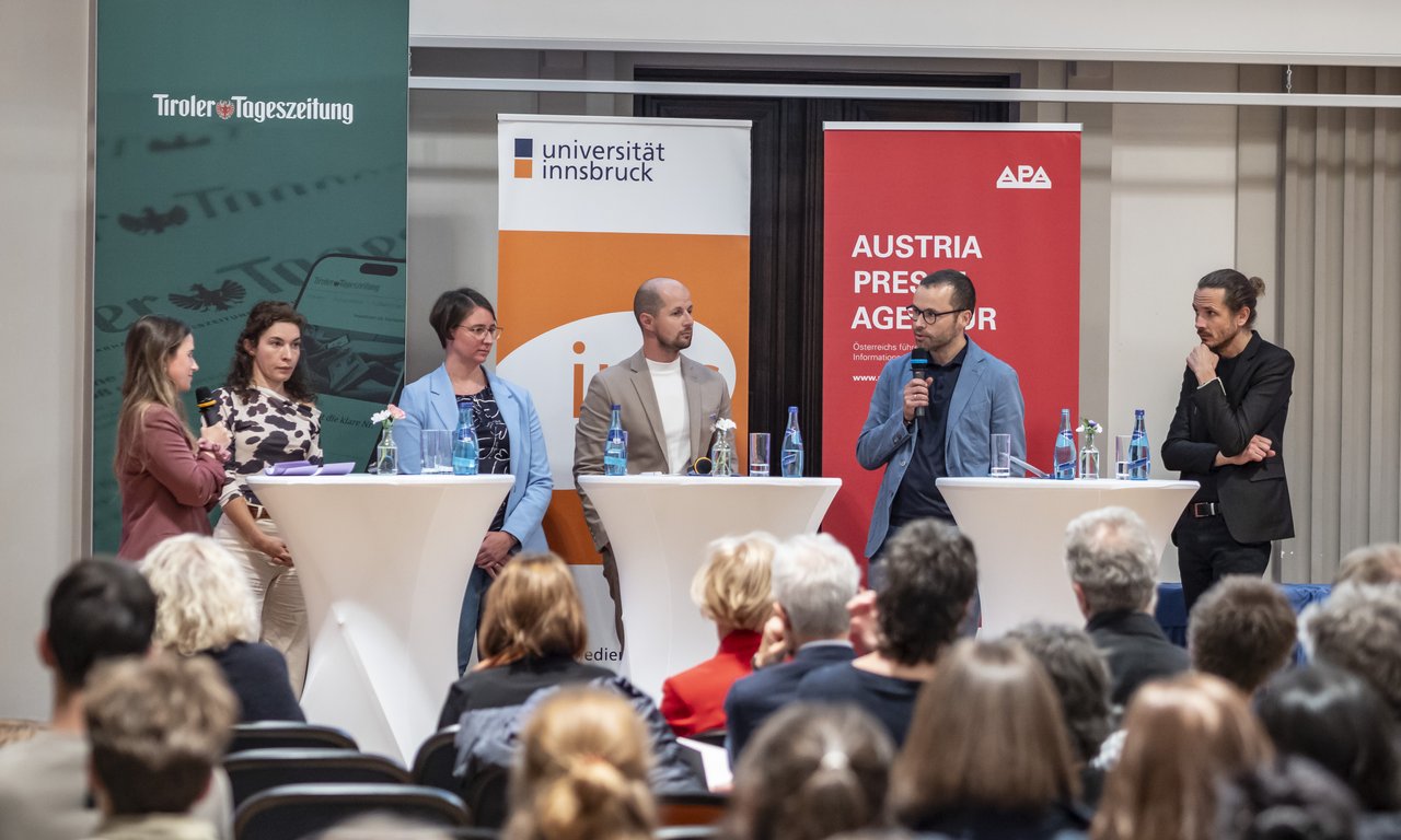 Mehrere Personen auf einer Bühne bei einer Podiumsdiskussion, dahinter Banner der Tiroler Tageszeitung, der Universität Innsbruck und der APA.