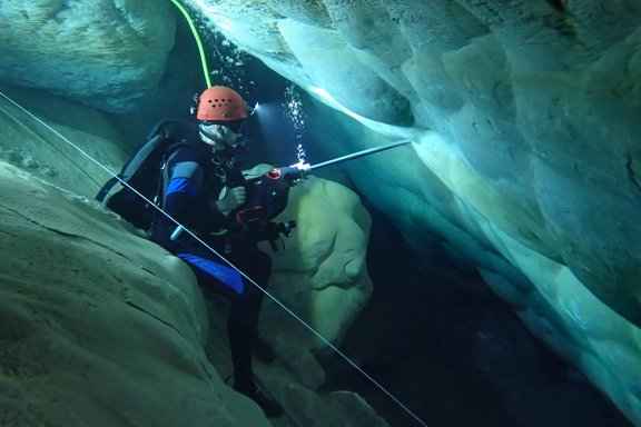 A diver takes cores from the cave wall with a drill.
