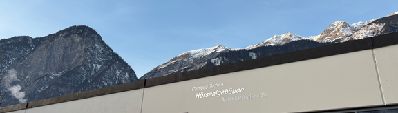 Blick auf das Hörsaalgebäude am Campus Technik, im Hintergrund die Berge