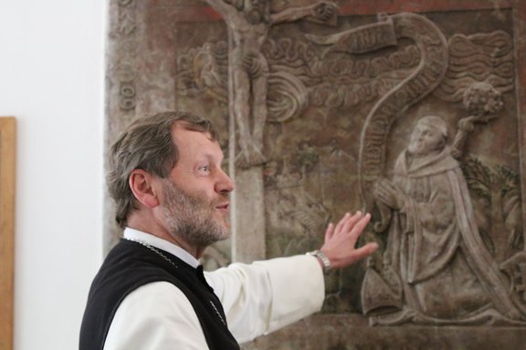 Der Abt zeigt auf ein altes Steinrelief