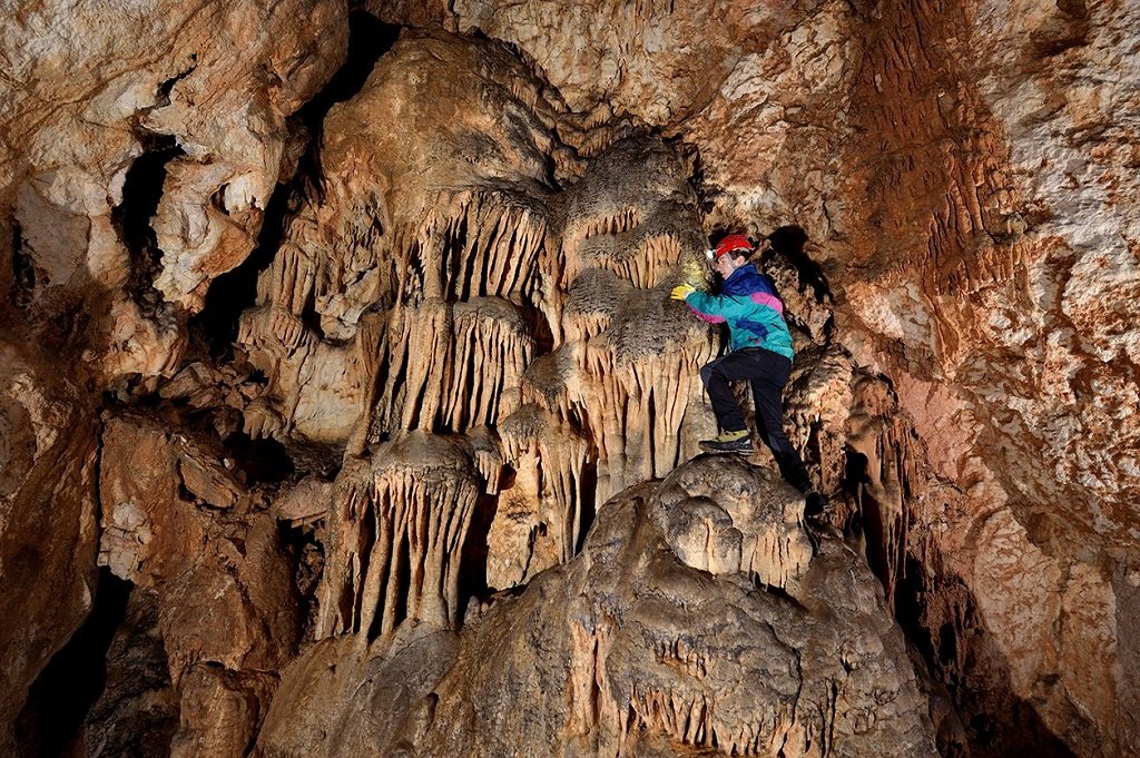 Eine Person in einer Höhle stehend und Tropfsteine untersuchend