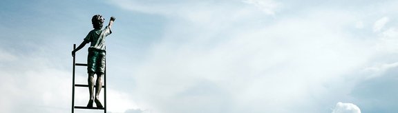 Statue: Kind auf einer Leiter greift zum Himmel