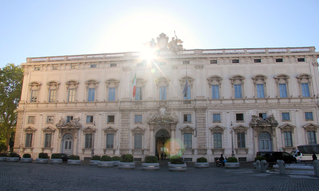 Foto des Gebäudes des italienischen Verfassungsgerichts, im Hintergrund blendet die untergehende Sonne.