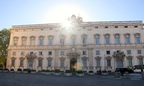 Foto des Gebäudes des italienischen Verfassungsgerichts, im Hintergrund blendet die untergehende Sonne.
