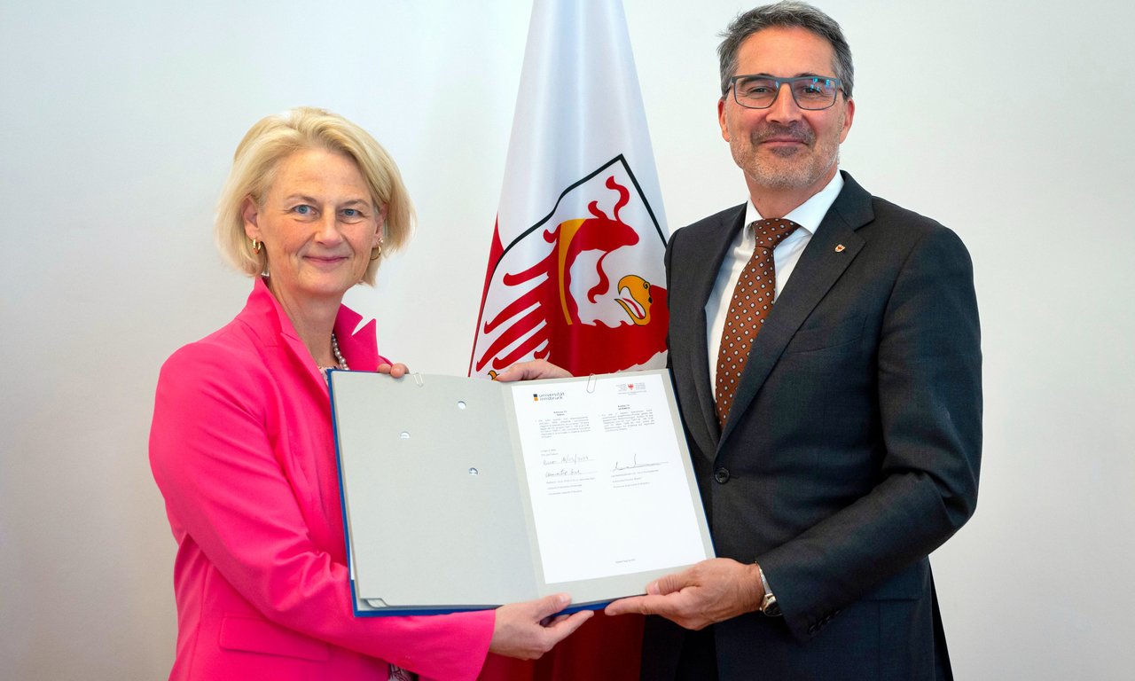 Zwei Personen halten gemeinsam ein Dokument in Händen und blicken in die Kamera