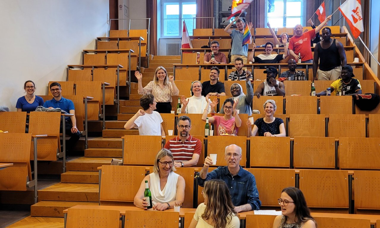 Zu sehen sind Personen im Hörsaal. Einige schwingen die Flagge Österreichs.