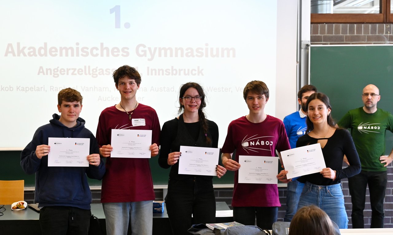 Fünf Schüler:innen mit Urkunden in der Hand stehen vor einer Leinwand