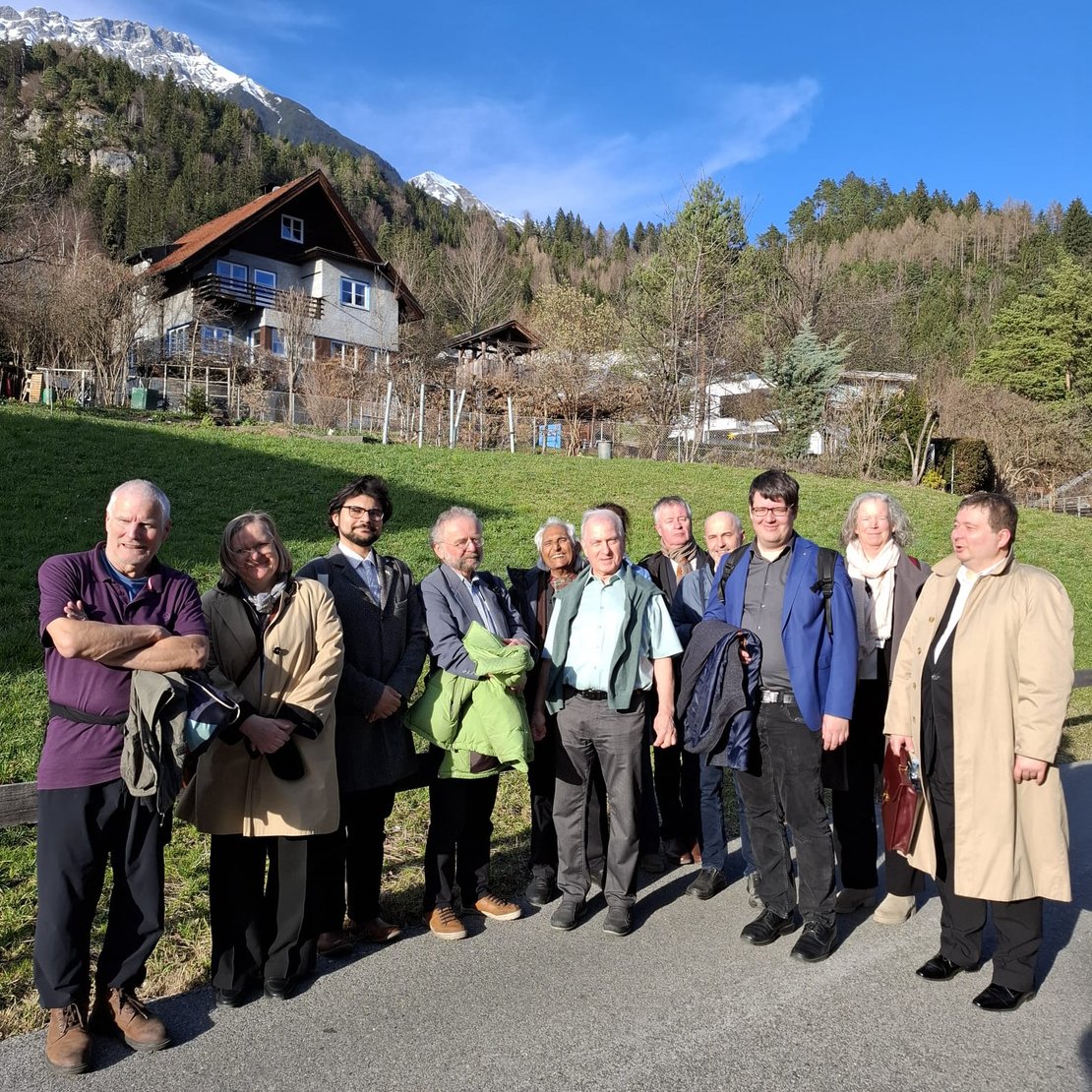 Zahhlreiche Personen stehen in einer Reihe und blicken in die Kamera, im Hintergrund Berge