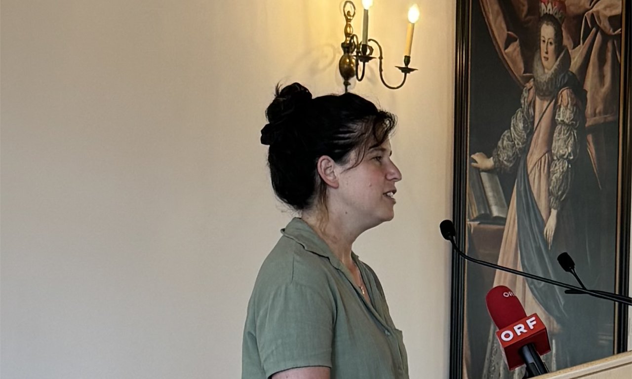 Frau bei einem Vortrag, sie ist von der Seite zu sehen, neben ihr ein altes Gemälde einer Frau.