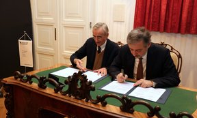 Zwei Männer sitzen an einem Tisch und unterschreiben Verträge
