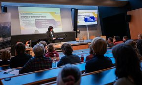 Hörsaal, Zuhörende von hinten, Votragende vor einer Powerpoint-Präsentation