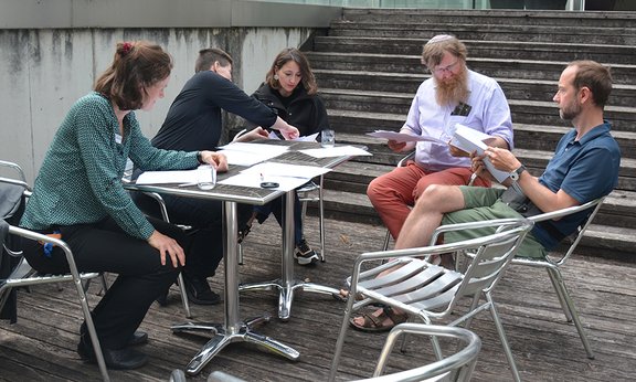 Personen sitzen um einen Tisch und studieren ihre Unterlagen