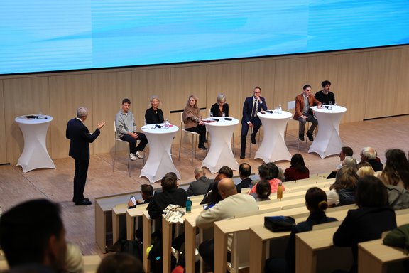 Mehrere Personen sitzen auf Barhockern an Bartischen und diskutieren.