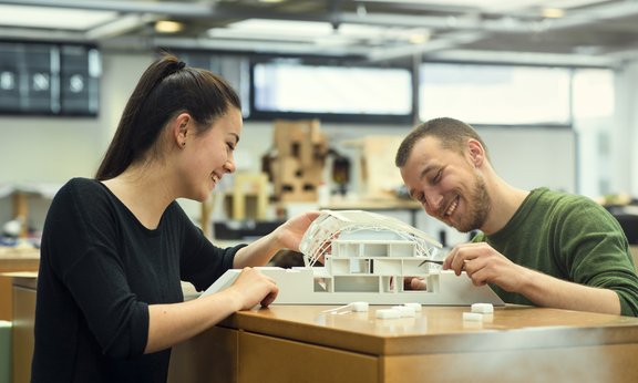 Zwei Personen bauen an einem Modell eines Gebäudes