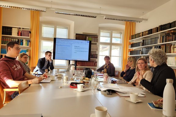 Zu sehen sind die Mitglieder des Instituts für Praktische Theologie. Sie sitzen an einem großen Tisch und unterhalten sich.