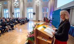 Rektorin hinter dem Redner:innenpult, vorne Publikum