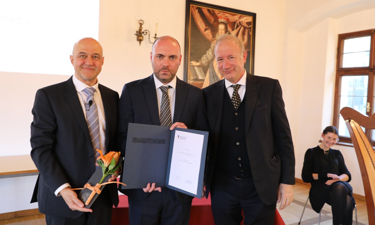 Group photo with three people. The award winner in the middle holds his certificate in his hands.