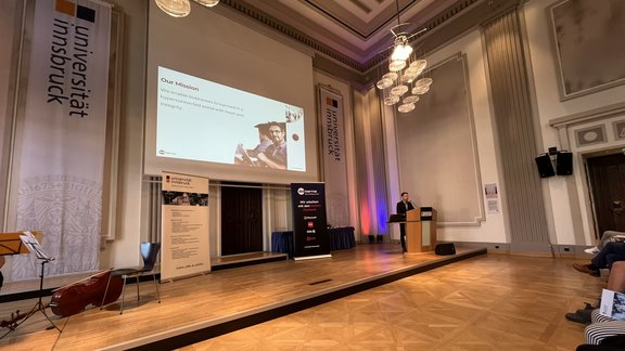 Image of a hall with an image presentation and a person at the lectern