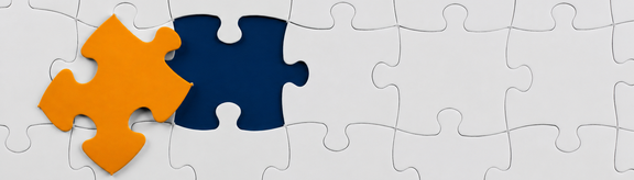 Weißes Puzzle mit einem orangen Puzzlestück, das noch fehlt