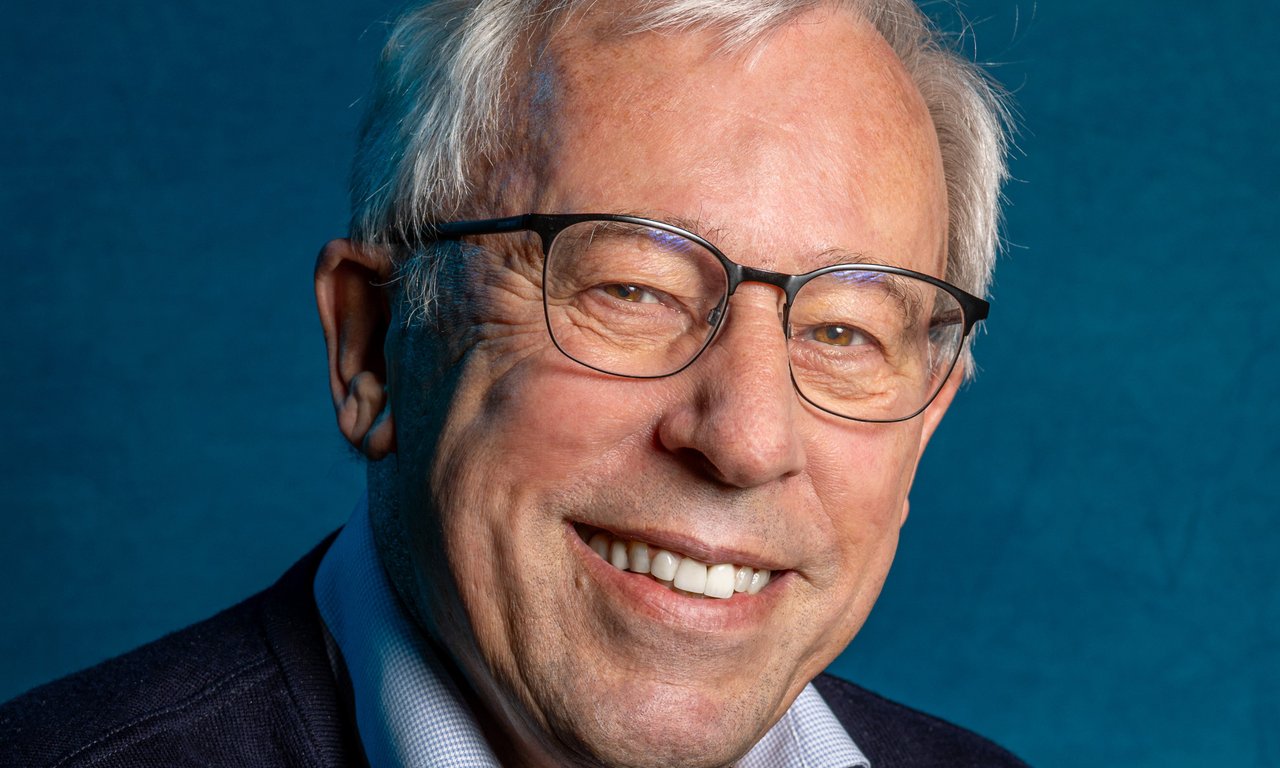 Porträtfoto von Peter Zoller vor dunklem Hintergrund. Er trägt eine Brille, sowie ein helles Hemd und einen dunklen Pullover