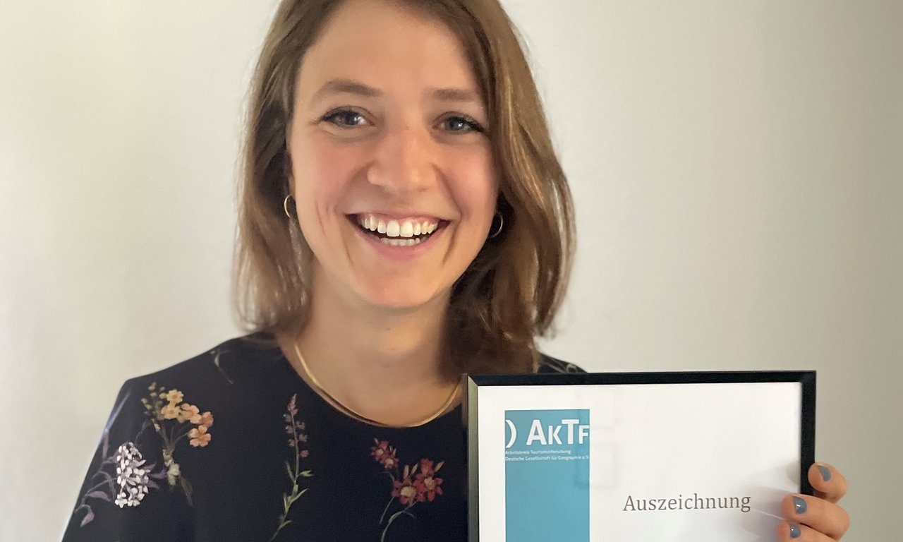 Eine Frau hält eine Urkunde und lächelt.