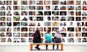 Symbolbild: Drei Menschen sitzen auf einer Museumsbank und schauen auf eine Vielzahl an Fotos von Menschen unterschiedlicher Hautfarbe und unterschiedlichen Geschlechts