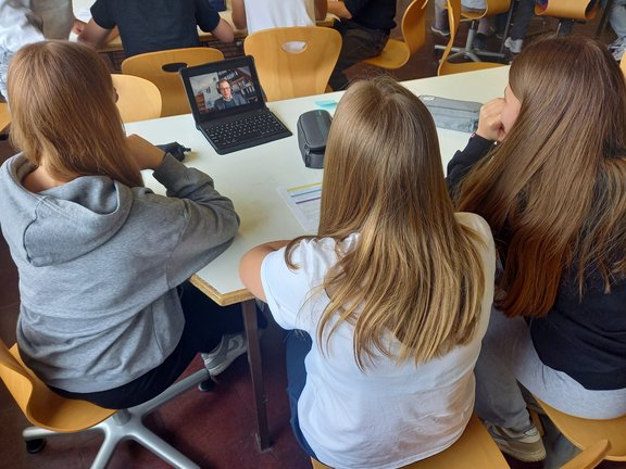 Jugendliche sitzen um einen Laptop, auf dem ein Videocall läuft.