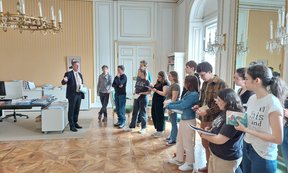 Eine größere Studierendengruppe steht in einem großen Raum in der Wiener Hofburg, ein Mann spricht mit den Studierenden.