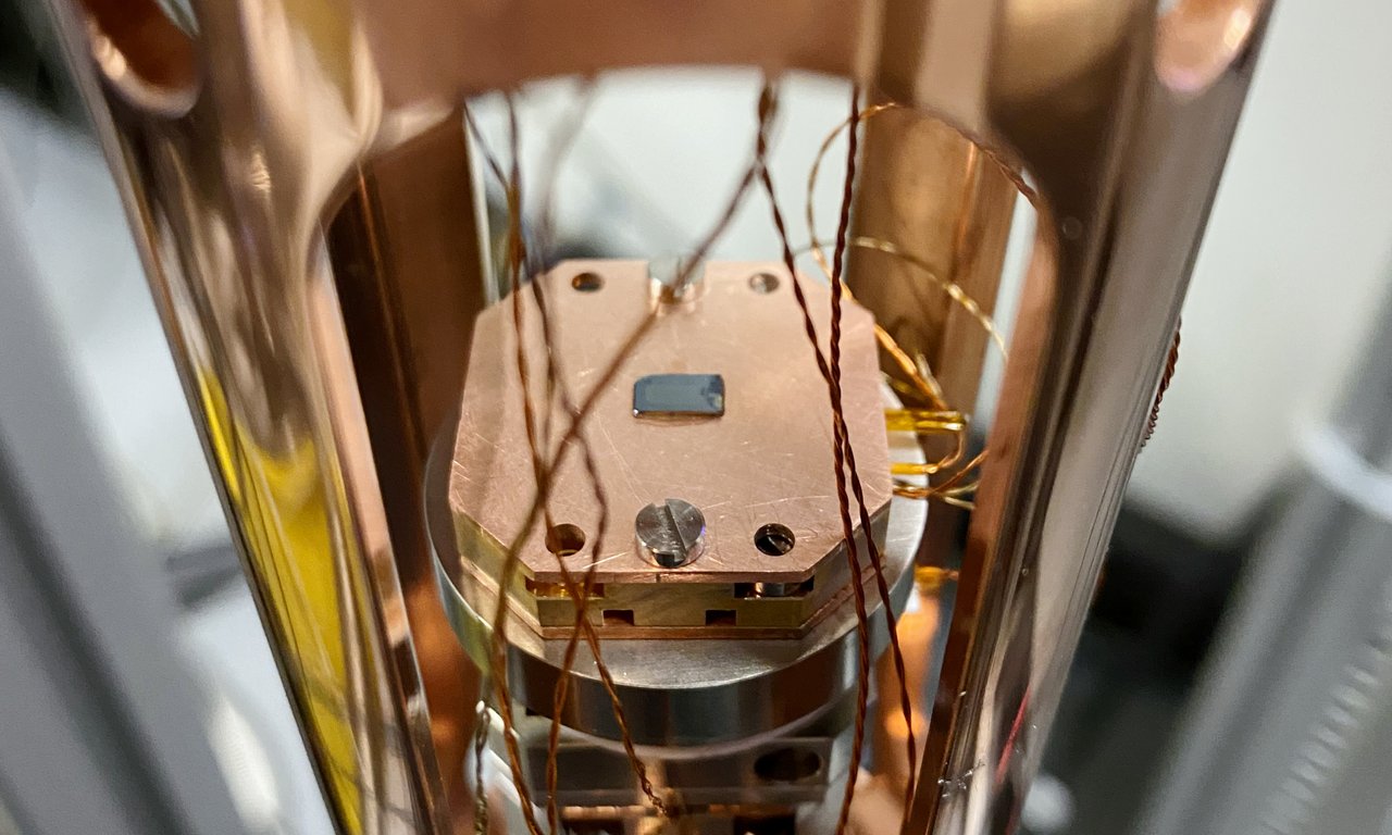 A cylindrical, shiny copper container with a semiconductor chip in the center to which cables lead.