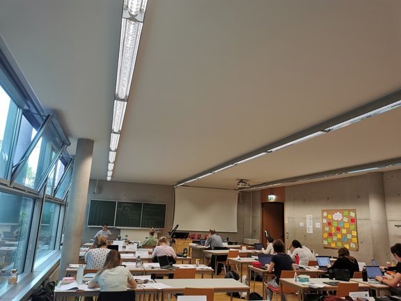 Studierende sitzen in einem Seminarraum und arbeiten an ihren Laptops