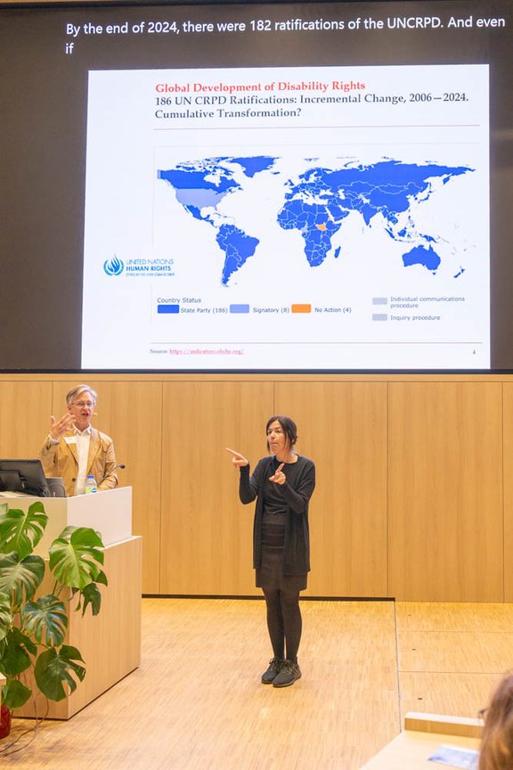 Zwei Menschen im Auximax stehend vor einer an die Wand projizierte Weltkarte