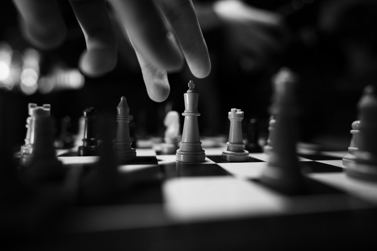 Schwarz-weiß Foto einer Hand, die eine Schachfigur auf einem Schachbrett absetzt