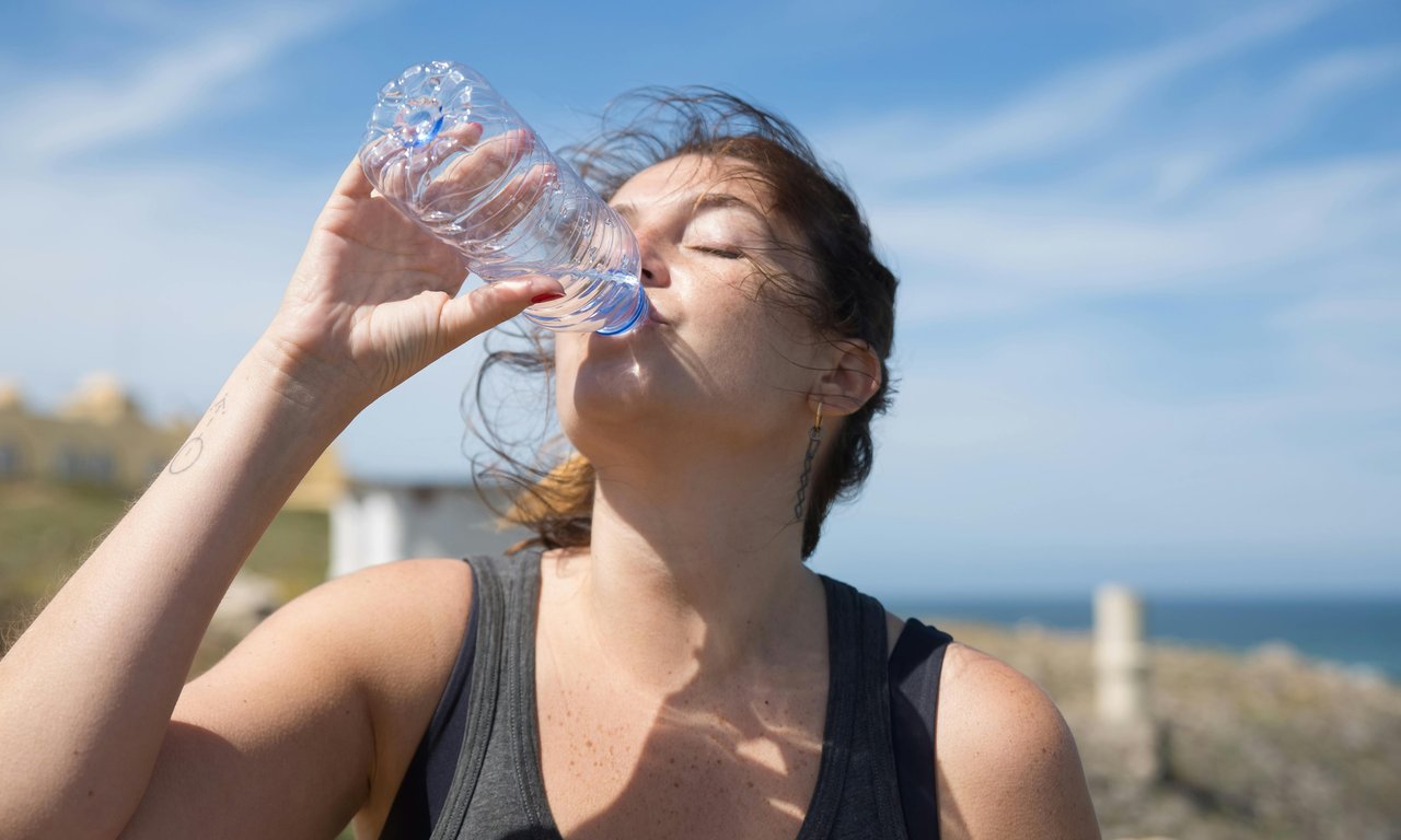 Frau mit blauem Himmmel im Hintergrund, die Wasser trinkt