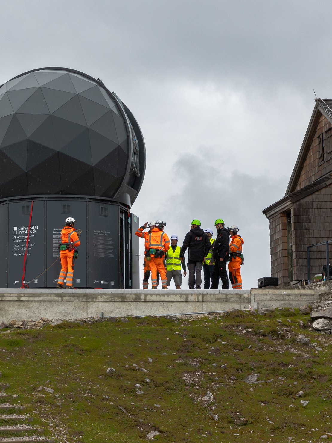 Die fertig montierte Bodenstation, schwarzer Unterbau, schwarze Kuppel, und Montagepersonal