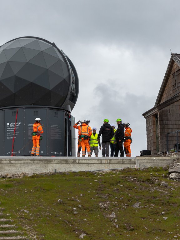 Die fertig montierte Bodenstation, schwarzer Unterbau, schwarze Kuppel, und Montagepersonal