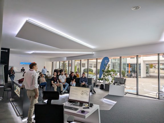 zeigt den Raum mit allen Teilnehmer:innen von der Seite