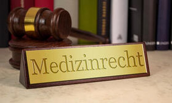 Anwaltshammer mit Tischkarte im Vordergrund mi der Aufschrift "Medizinrecht"